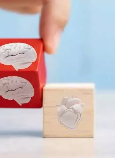 Mão posicionando blocos com ícones de cérebro e coração, simbolizando o equilíbrio entre razão e emoção — essência da inteligência emocional.