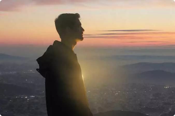 Homem com vestes filosóficas sentado diante de uma cidade dourada ao pôr do sol, simbolizando a solidão e a reflexão de quem desperta para a consciência.