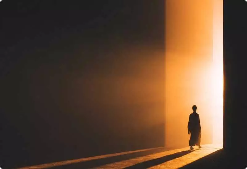Pessoa caminhando da escuridão para uma luz dourada, simbolizando o despertar da consciência e o caminho do autoconhecimento.
