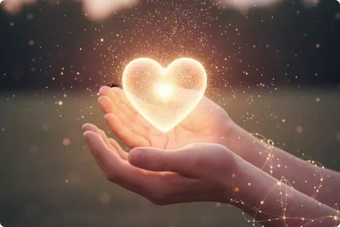 Mãos segurando um coração luminoso simbolizando gratidão e bem-estar emocional.
