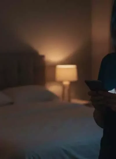 Mulher usando celular à noite no quarto, ilustrando a exposição à luz artificial à noite e o risco cardíaco associado ao uso de telas antes de dormir.