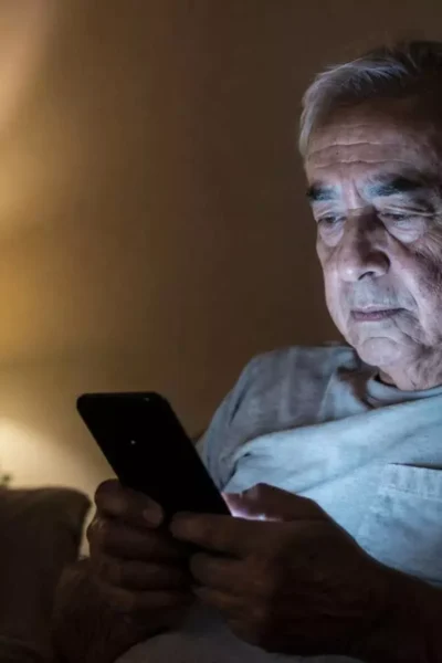 Idoso usando celular à noite, representando o uso excessivo de telas em idosos e seus impactos no sono e na saúde mental.